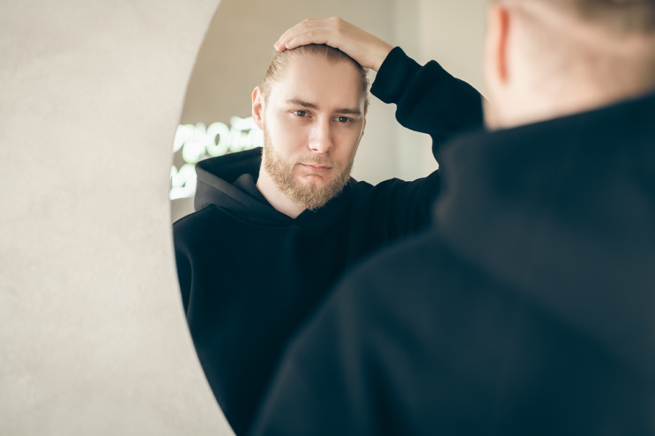 An attractive young man with a beard looks at himself in the mirror.